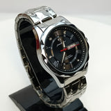 Silver watch with black face on a reflective surface