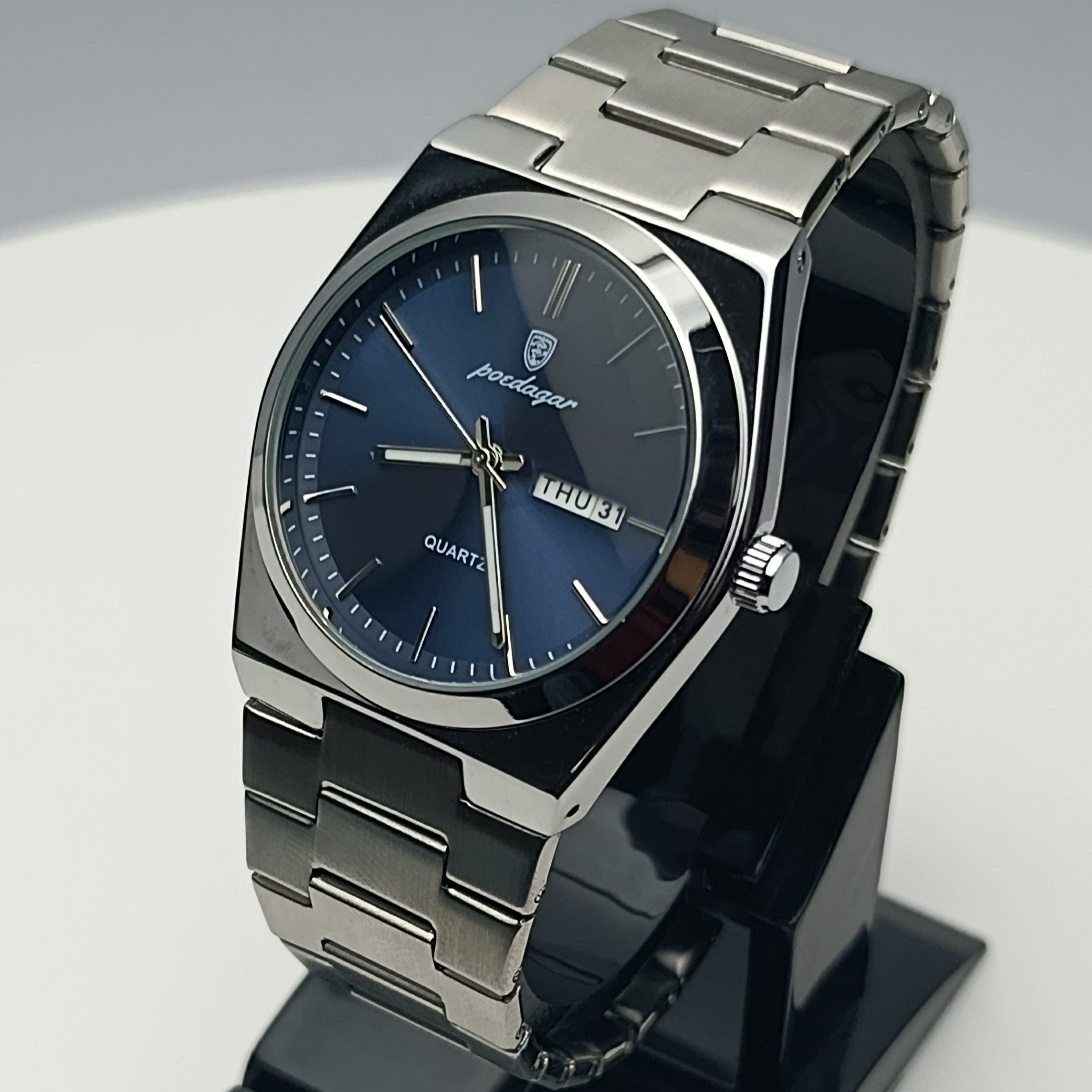 Silver watch with blue face on a black stand against a gray background