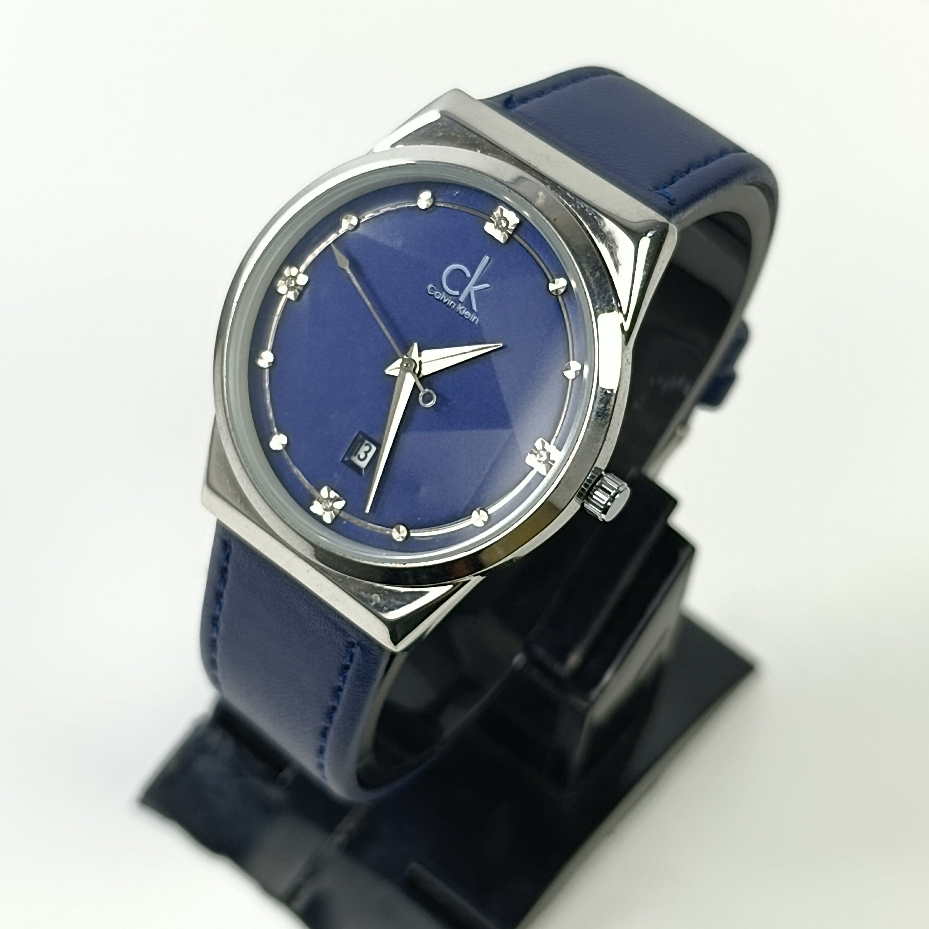 Blue watch with silver case on a black stand against a white background